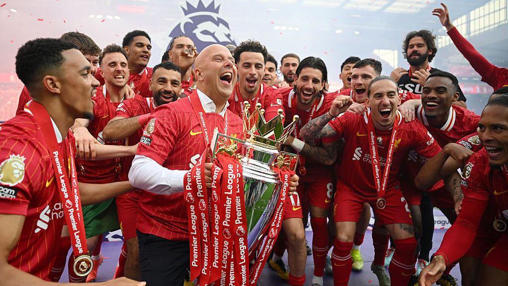 Arne Slot lifts the Premier League trophy surrounded by his players 