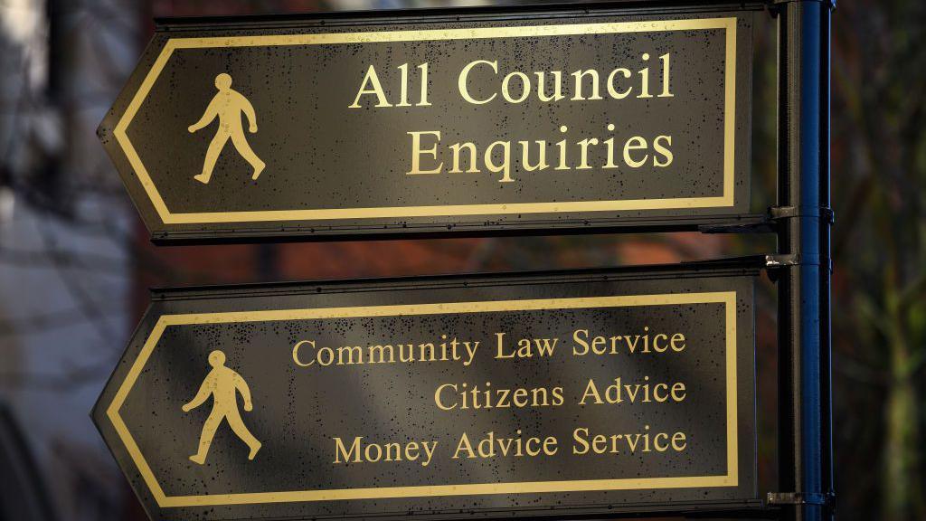 Two black arrow signs, with gold writing. One says "all council enquires" and the other points to various services. There are also two silhouettes of men on each sign to symbolise walking.