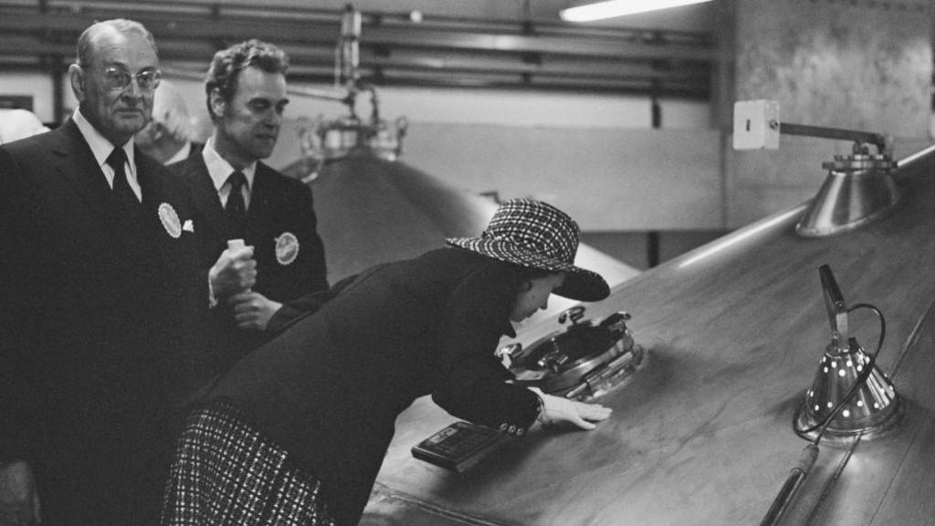 Princess looking through an inspection window of a hopper while two men in suits watch