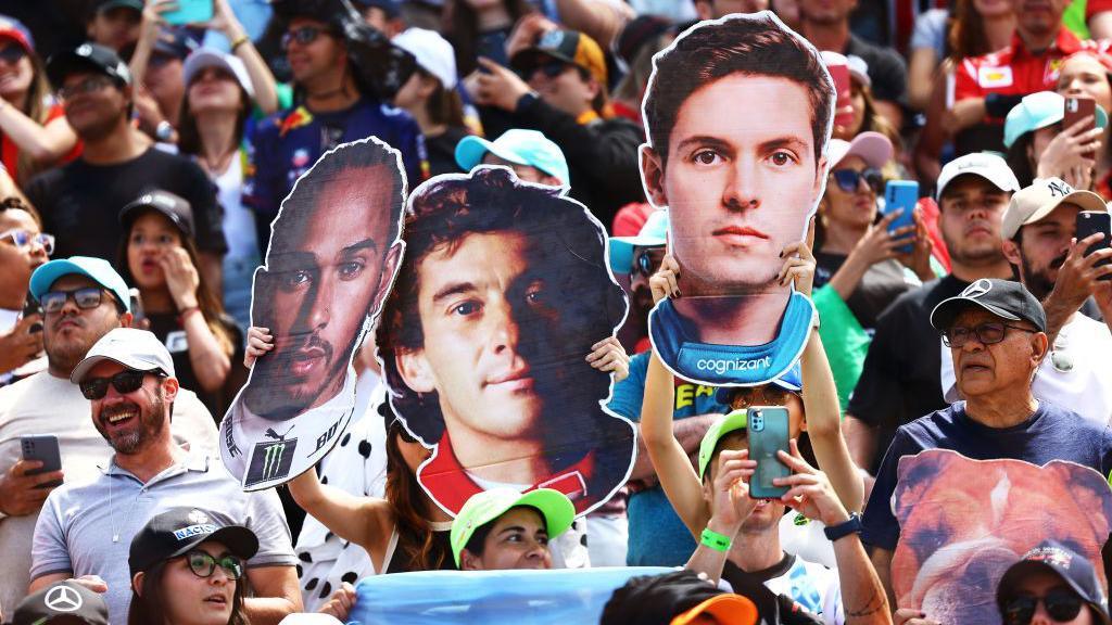 Fans hold up cardboard cutouts of Lewis Hamilton and Ayrton Senna 