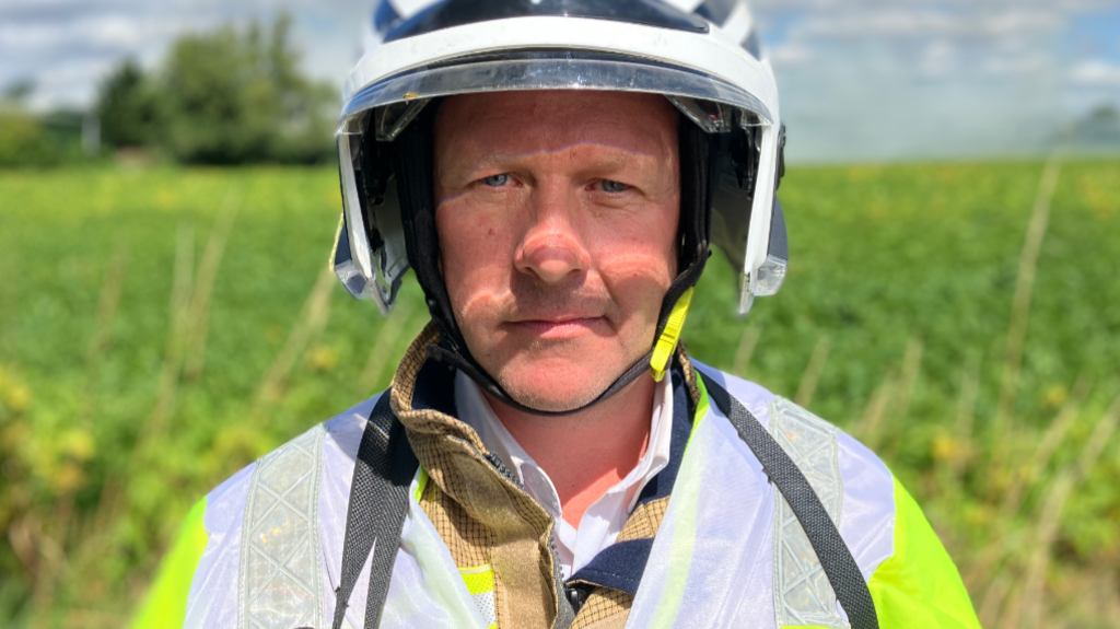 A firefighter wearing a white helmet looks towards the camera