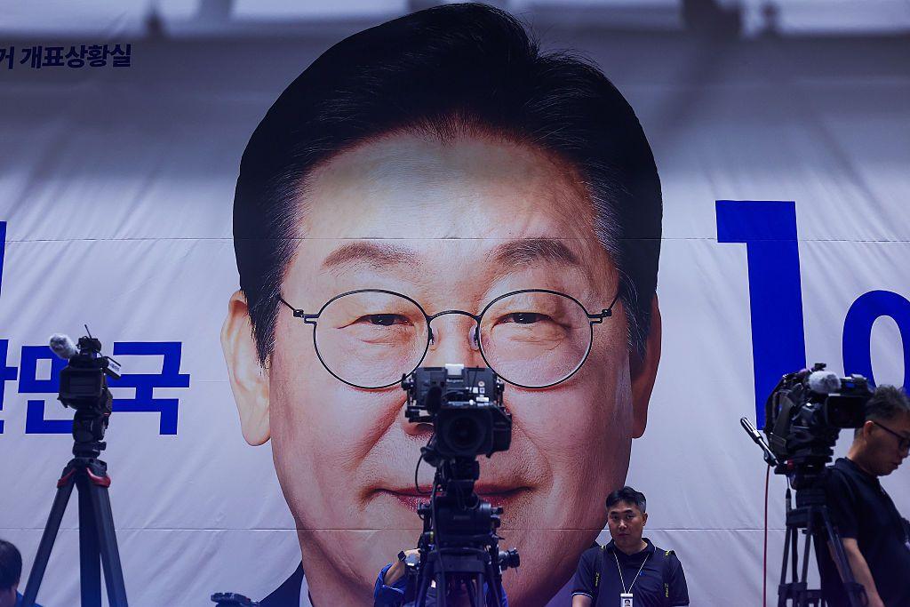 Cameras in front of a banner of Lee Jae-myung's face
