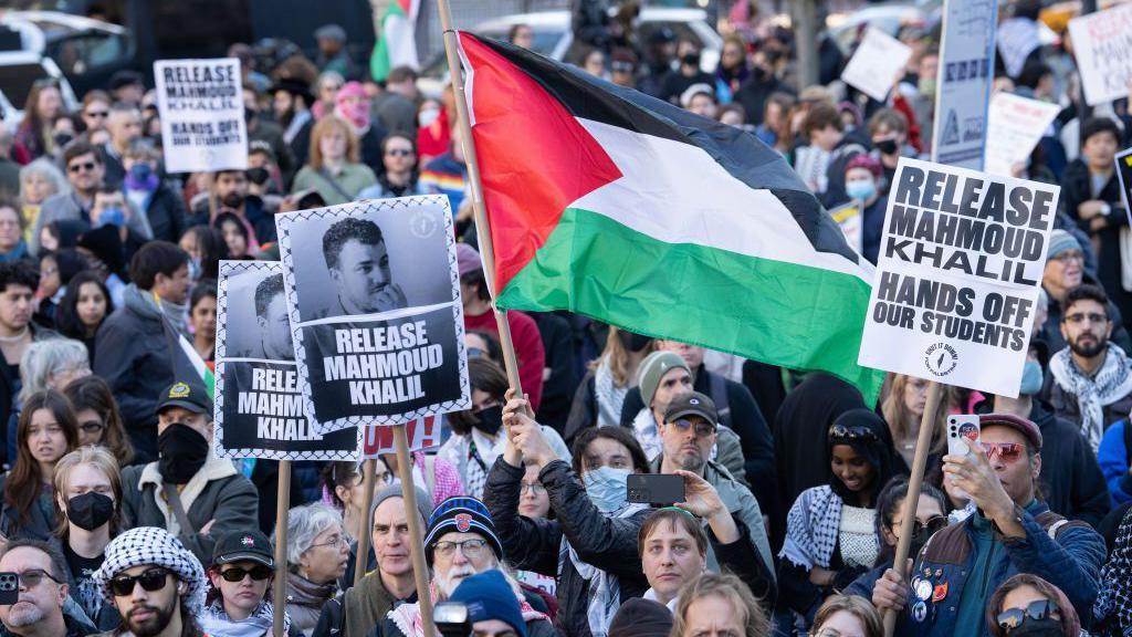 A crowd of protesters, some of whom carry Palestinian flags or signs calling for the release of Mahmoud Khalil