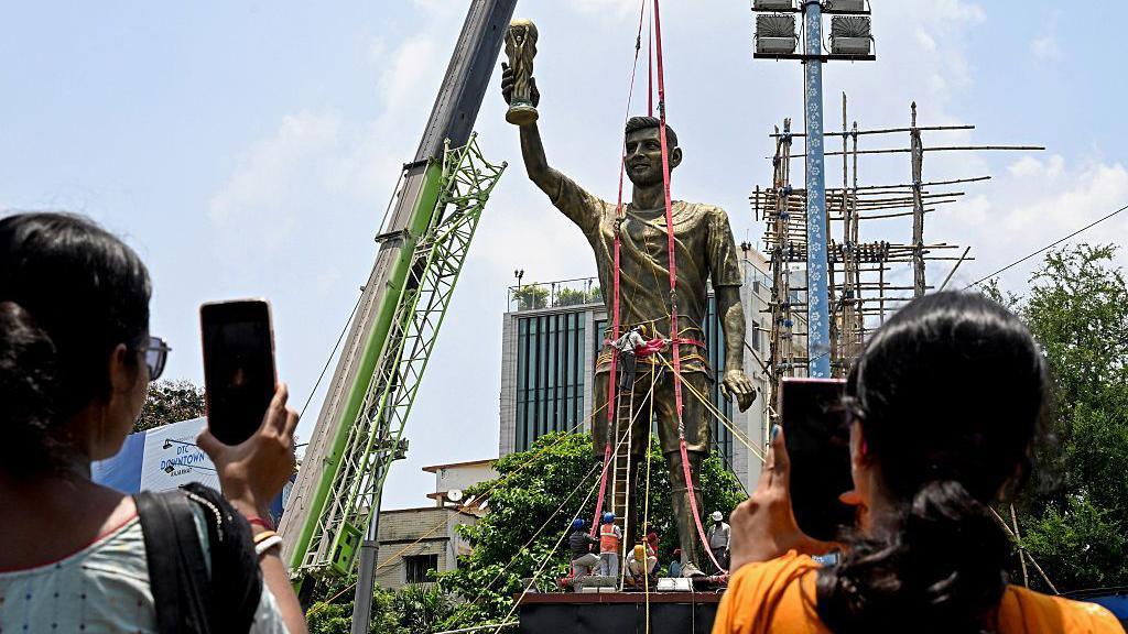 Pedestrians stop to take pictures of Lionel Messi's statue as removal begins.