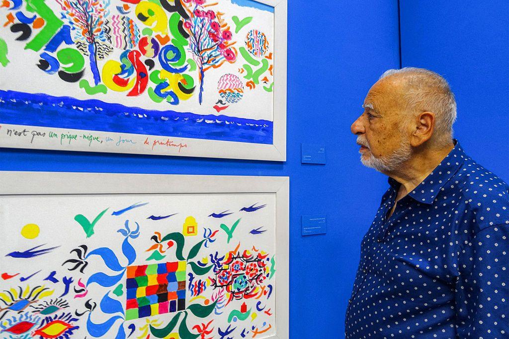 A man stands close to colourful paintings.
