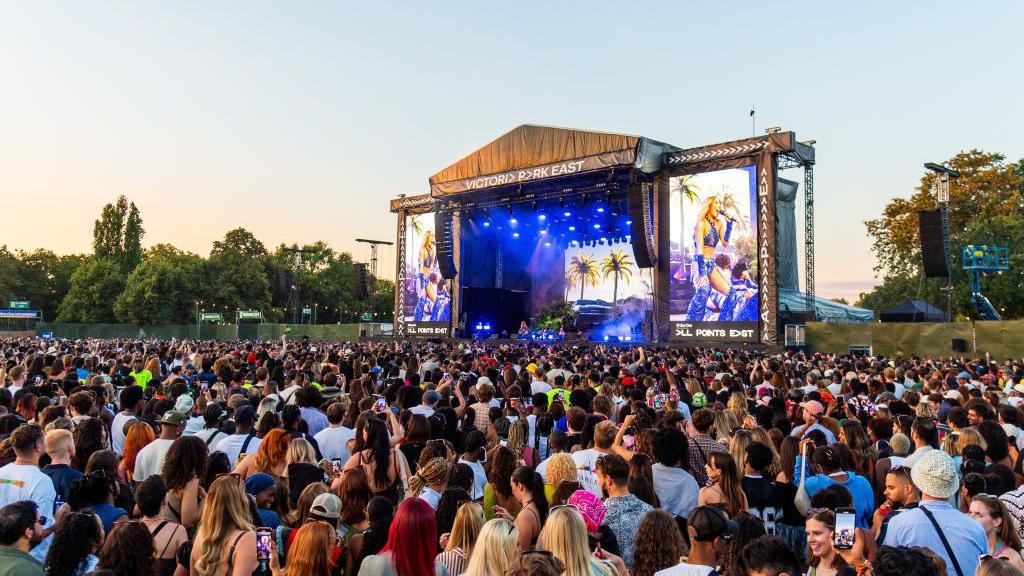 Crowd gathered in front of the main stage at All Points East festival in Victoria Park, London, watching a performance as large video screens display close-ups of the artist.