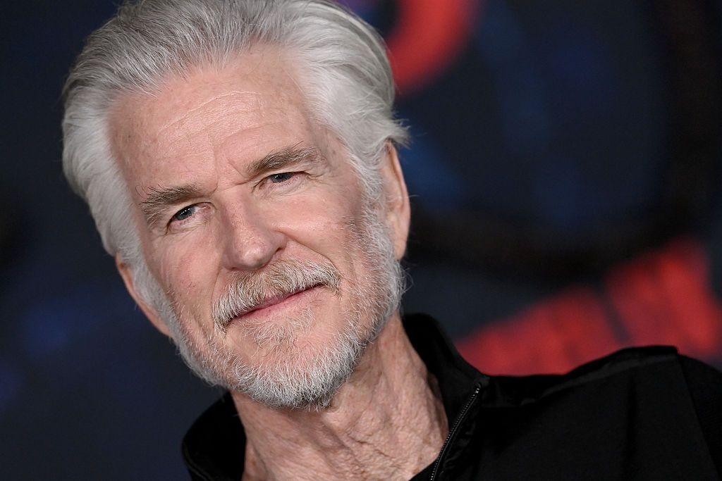 Actor Matthew Modine attends the Los Angeles Premiere of Netflix's "Stranger Things" Season 5 - he is an older man with white hair and stubble and he stands in front of a black backdrop with the Stranger Things logo.
