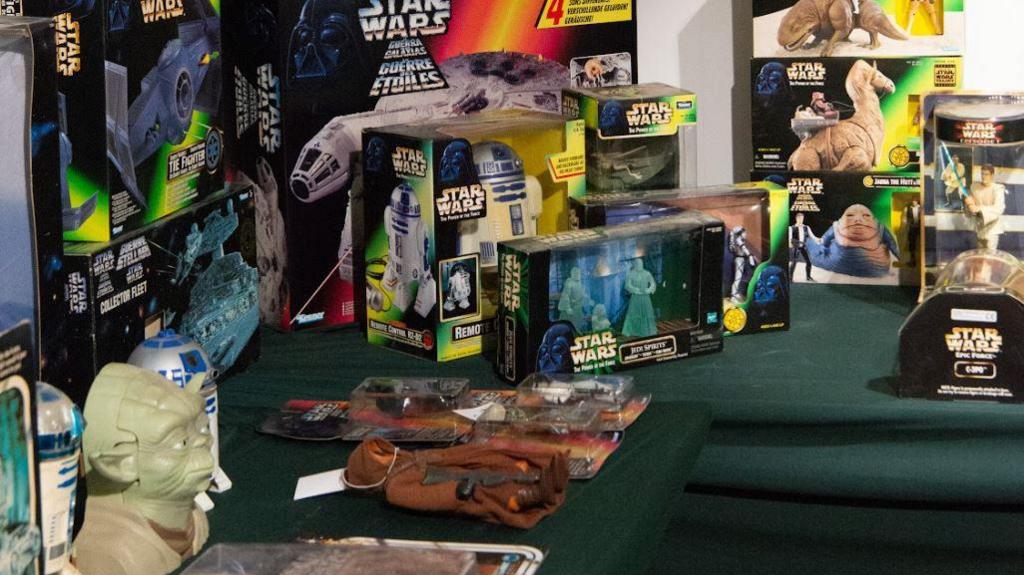 A collection of Star Wars memorabilia, including action figures and models of a variety of space vehicles. The items are on a green table. 