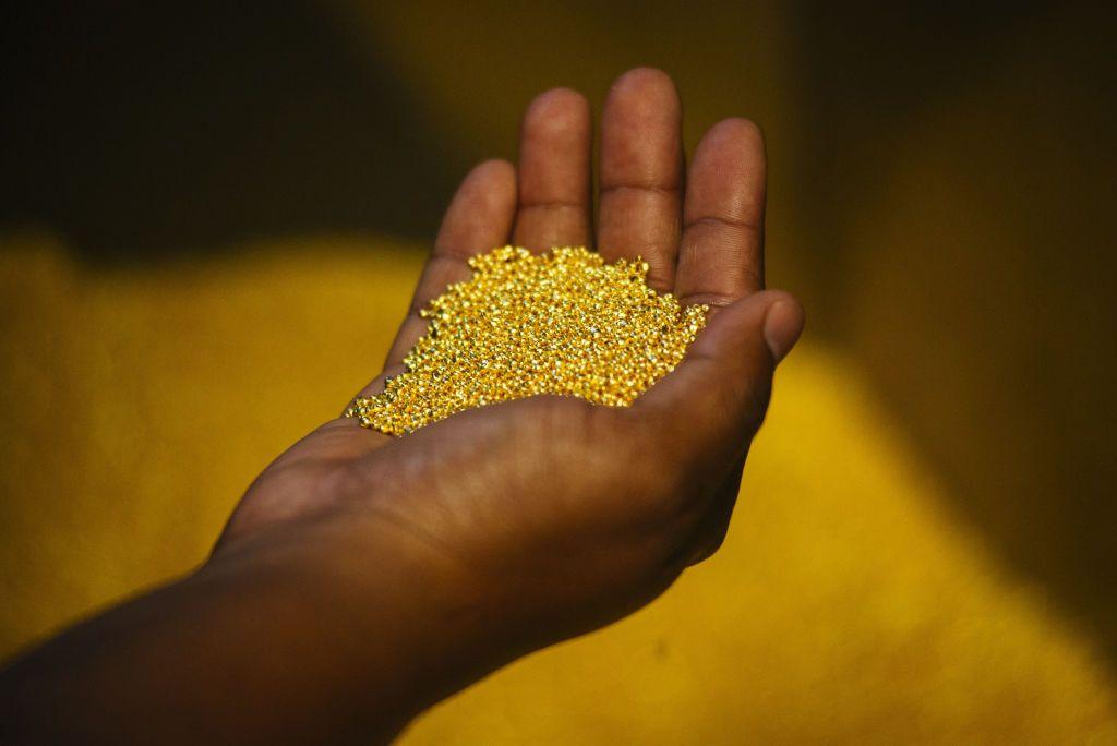 A worker at a mine in a different country holds a handful of gold bullion granules.