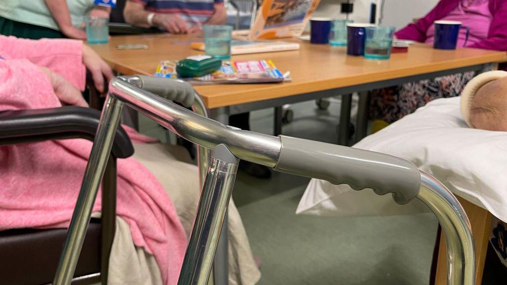 A stock image of a zimmer frame in a care home. There are also several elderly people in the photo.