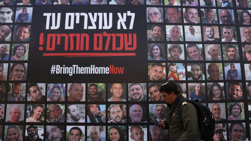 A man walks past a poster displaying dozens of people taken hostage by Hamas into Gaza.