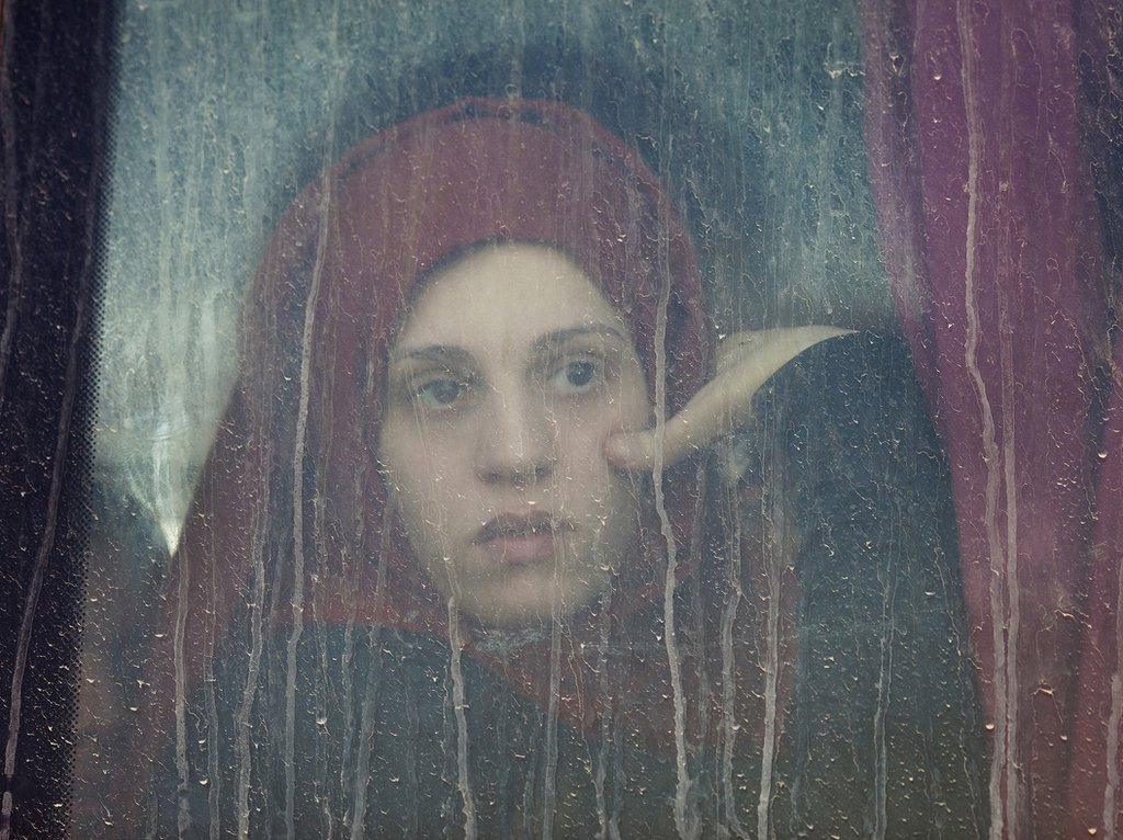 A young woman looks out of a window of a bus