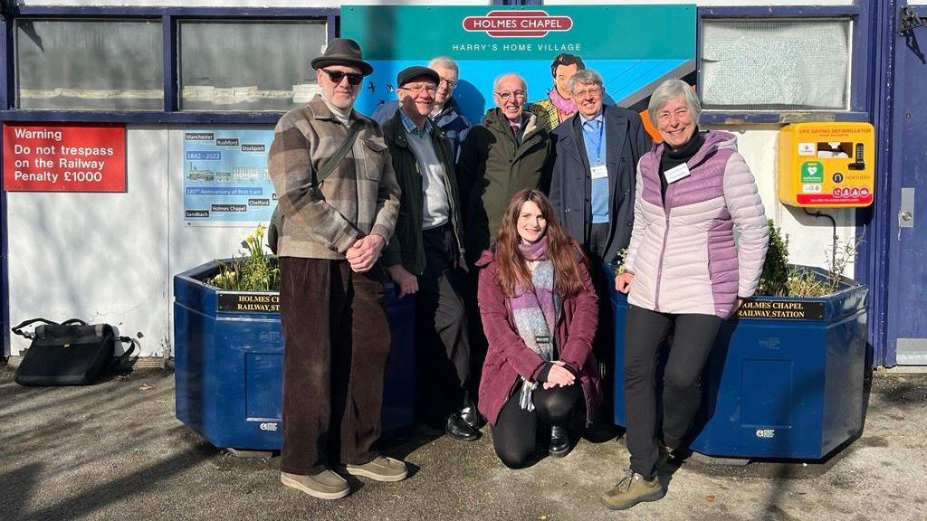 Eamonn Murphy (left) and Victoria Turner (centre) pose in a crowd of four other people in front of the platform mural.