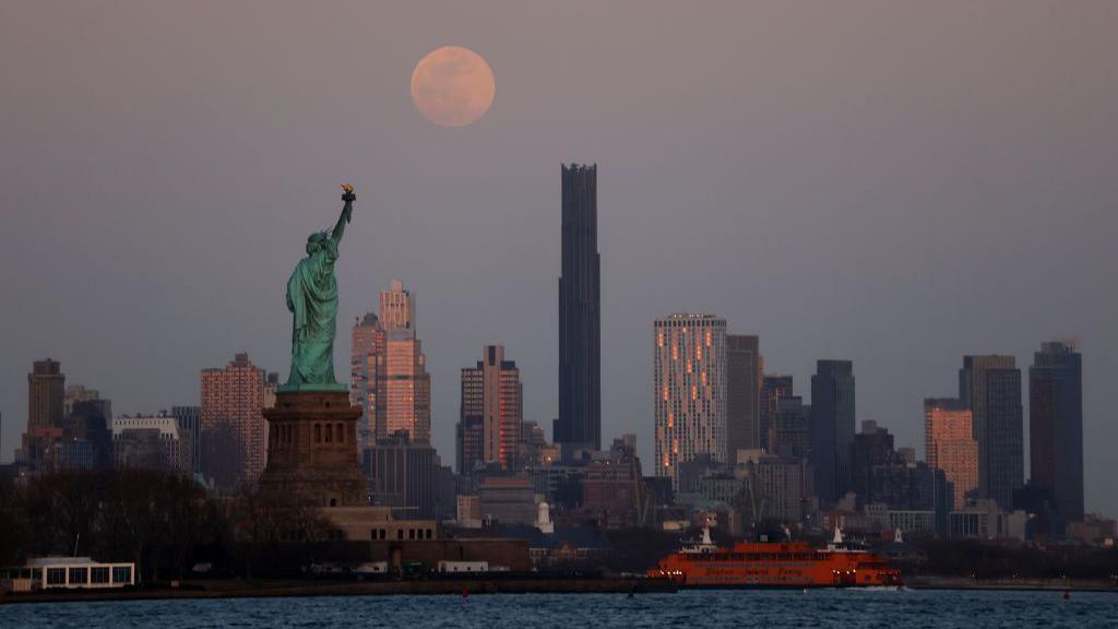 The Moon is seen behind the Statue of Liberty in New York City.