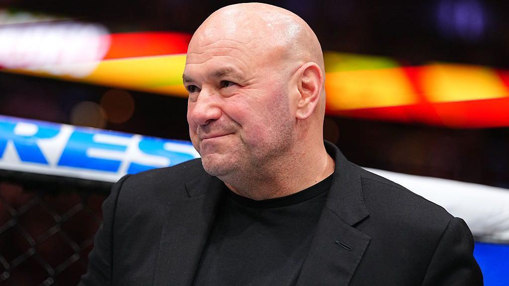 Dana White smiles and is wearing a black jacket
