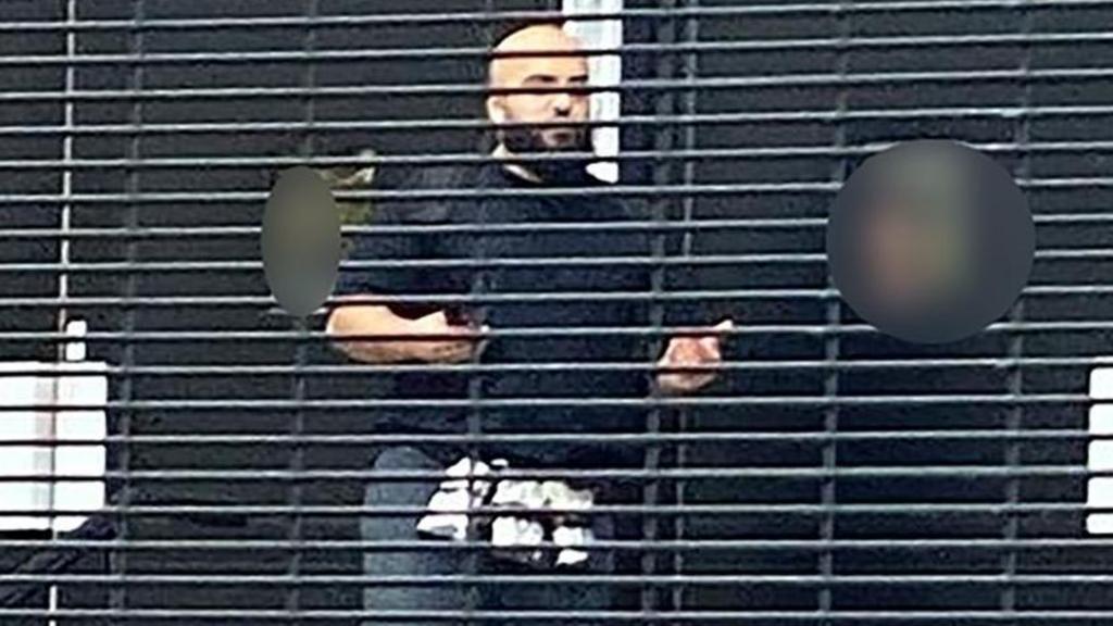 Suspect in attack with items trapped round his waist. He is bald with a beard and is wearing a dark jumper and jeans