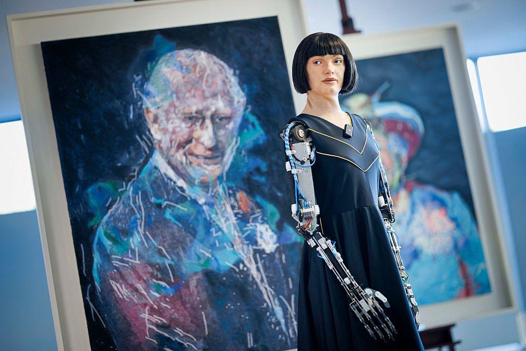 humanoid robot ai-da stands wearing a formal black dress looking into the distance in front of her portraits of king charles iii and queen elixabeth ii