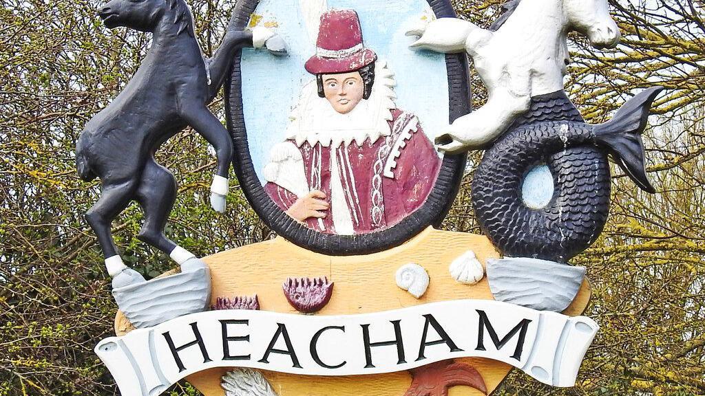 We can see the Heacham village sign. In the centre is a young woman dressed in typical Elizabethan attire. Across the bottom it says 'Heacham'.