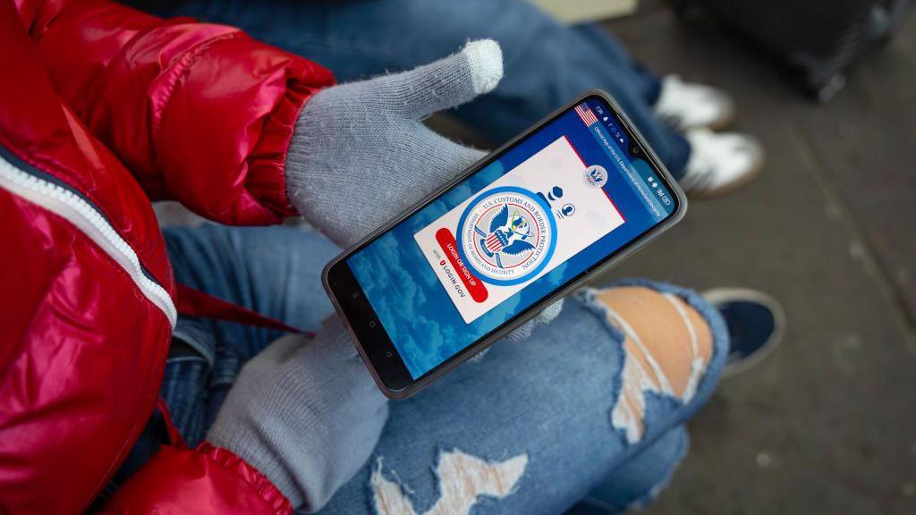 File image of an anonymous hand holding a phone that displays the CBP One app