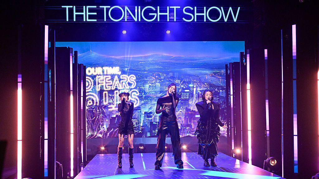EJAE, Audrey Nuna and Rei Ami performing Golden with 'The Tonight Show' in big neon letters above them