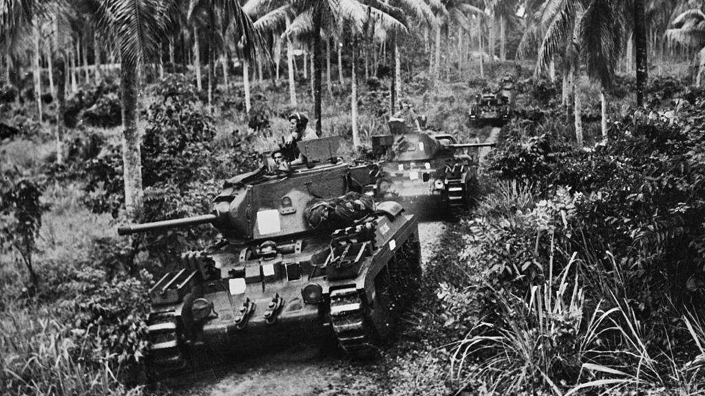 Tanks with soldiers onboard driving through a jungle.