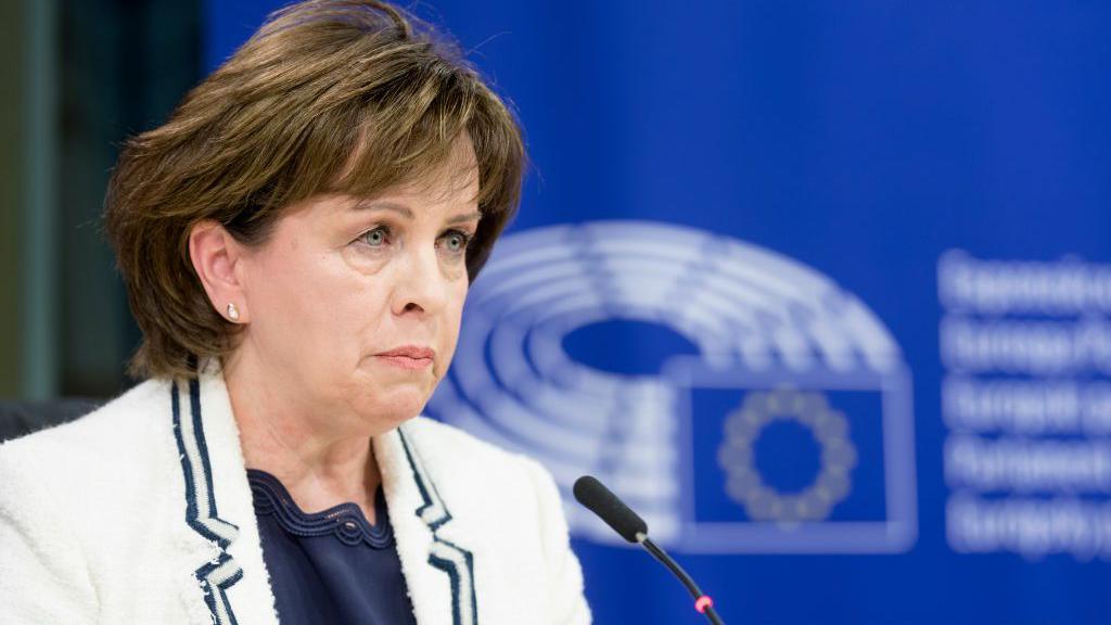 Diane Dodds in a white blazer with navy trim and a navy top, pictured speaking into a microphone at the European Parliament in 2018