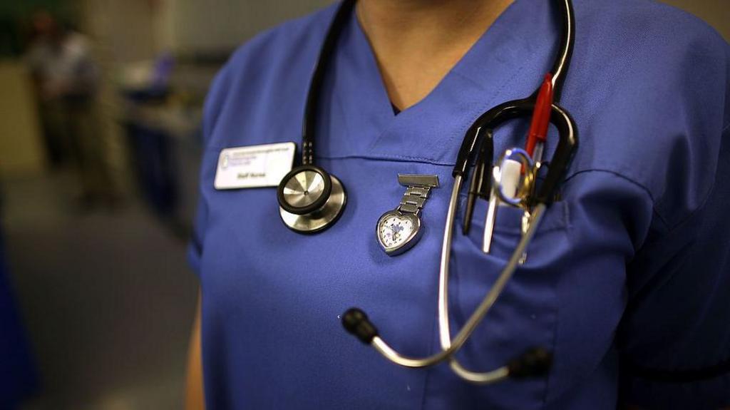 A close up photo of a nurses uniform, decorated with a name badge, watch and stethoscope