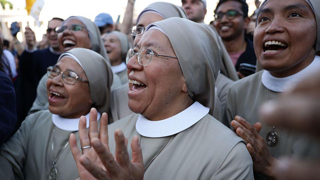 A group of nuns dressed in grey look on with excitement as the new Pope addresses the crowd in St Peter's Square on 8 May 2025.