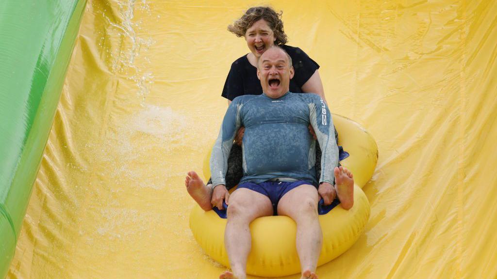 Sir Ed Davey and Anna Sabine, parliamentary candidate for Frome and East Somerset, ride the Ultimate Slip 'n' Slide at Eastcote Farm during an election campaign visit in Beckington