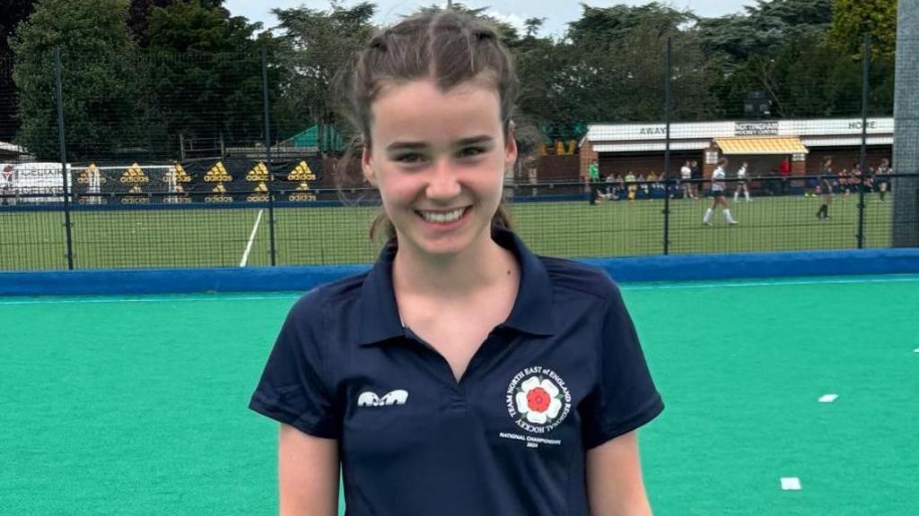 A young girl in a sports polo shirt standing on a hockey pitch