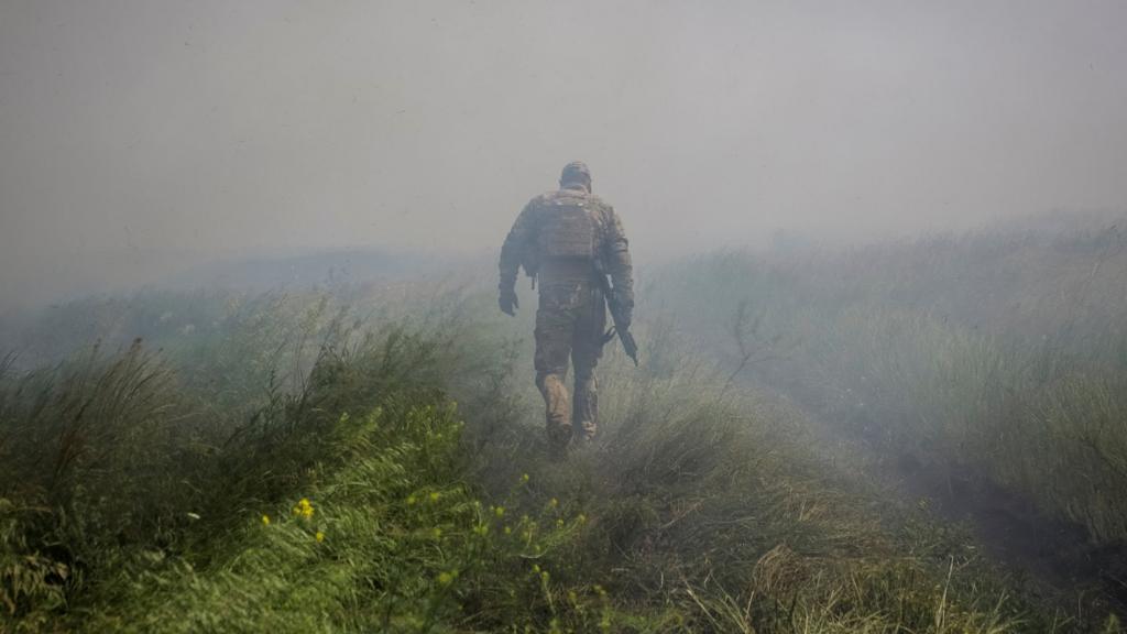 A Ukrainian soldier walks through a dusty field