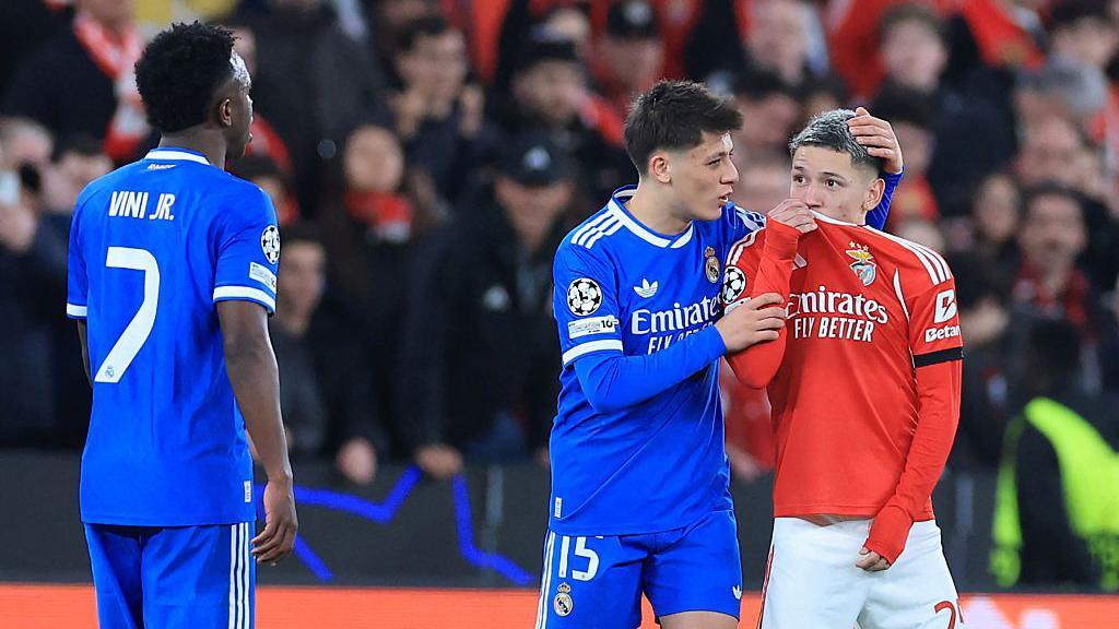 Gianluca Prestianni (right) lifts the collar of shirt over his mouth as he looks towards Vinicius Junior.