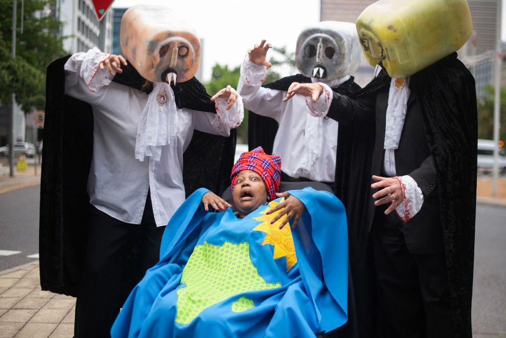 A protestor from Extinction Rebellion Cape Town (C), wearing clothes that represents Africa, is being threatened by 'Fossil Fuel Vampires' dressed in lawyers outfits during a demonstration against the ongoing use of fossil fuels, outside the venue where the Africa Oil Week Conference is being held.