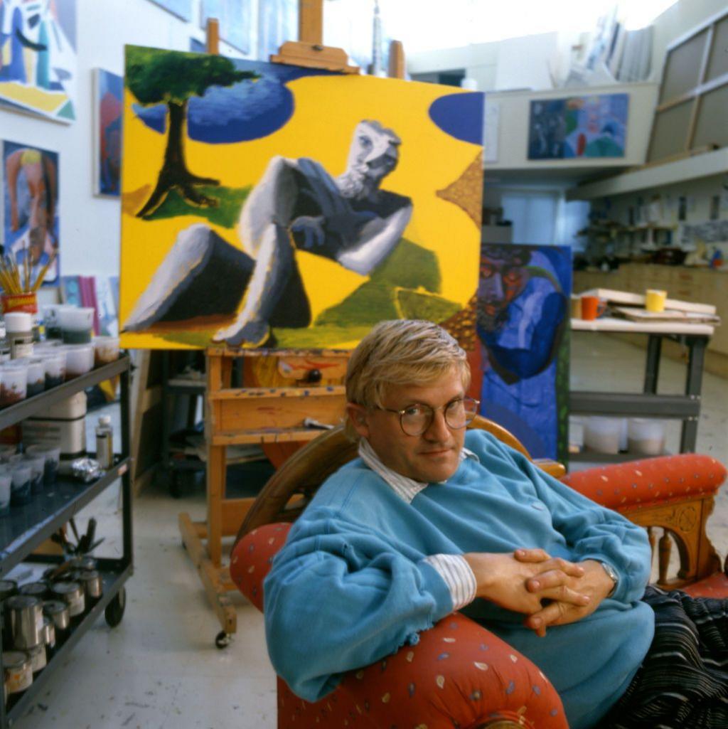 Portrait of English painter David Hockney, dressed in a light blue sweatshirt and tan trousers, as he sits on a chaise longue in his home, Los Angeles, California, 1987.