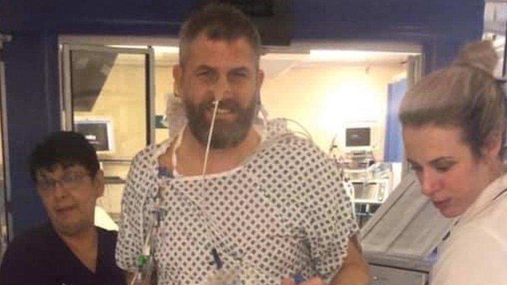 Stuart Cock in hospital gown with two members of hospital staff