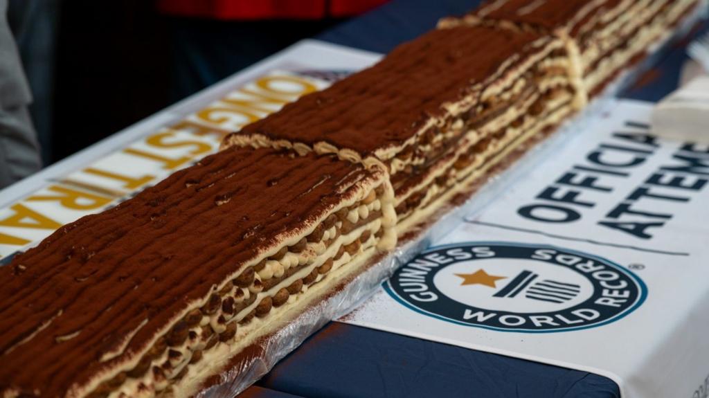 A very long tiramisu on a table which has the Guinness World Record logo upon it