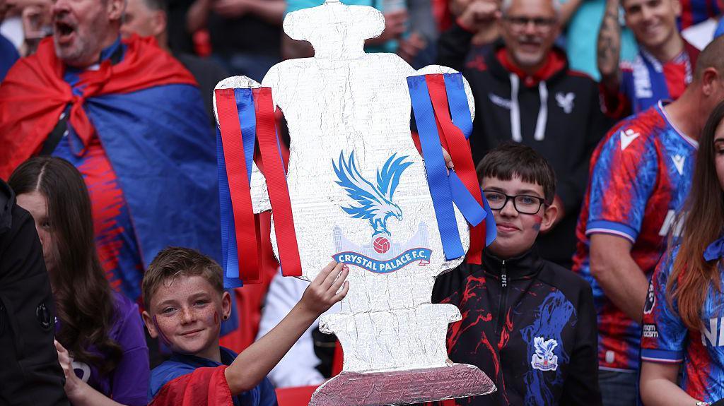 Two young Crystal Palace fans hold aloft their home made FA Cup trophy.