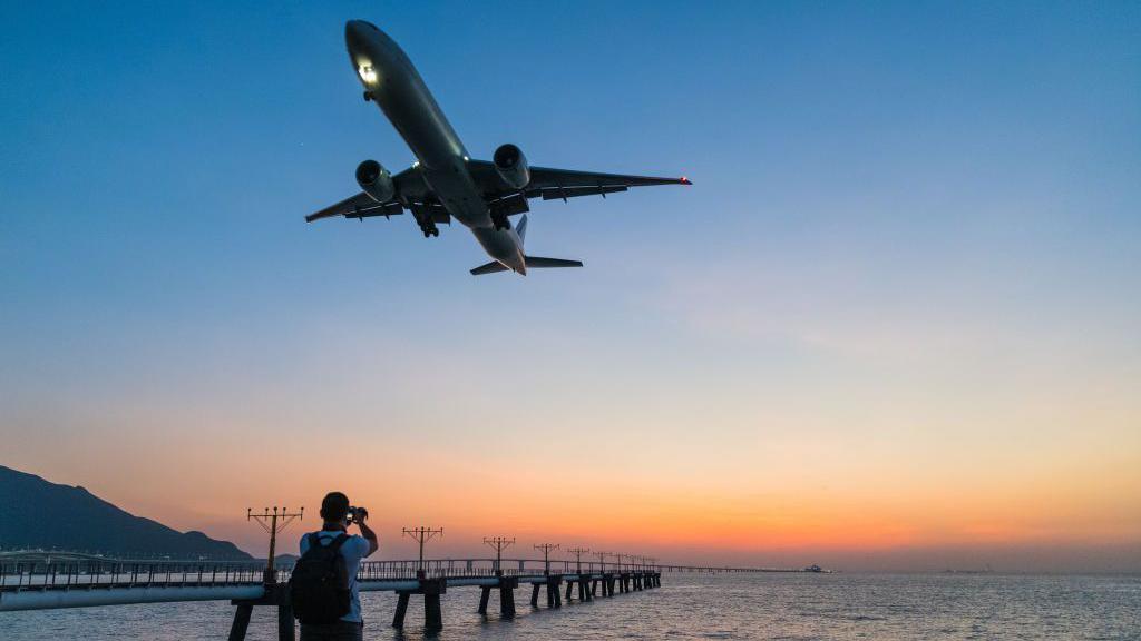 A person takes a photo of a plane flying overhead