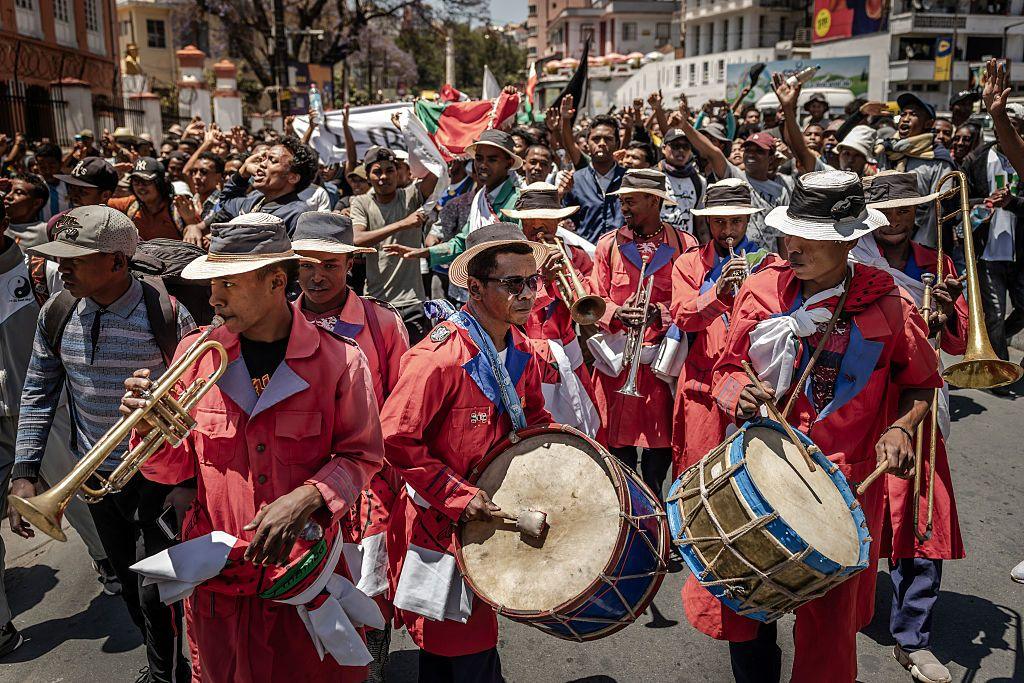 Protesters dance and smile behind a marching bad who wear matching red clothes.