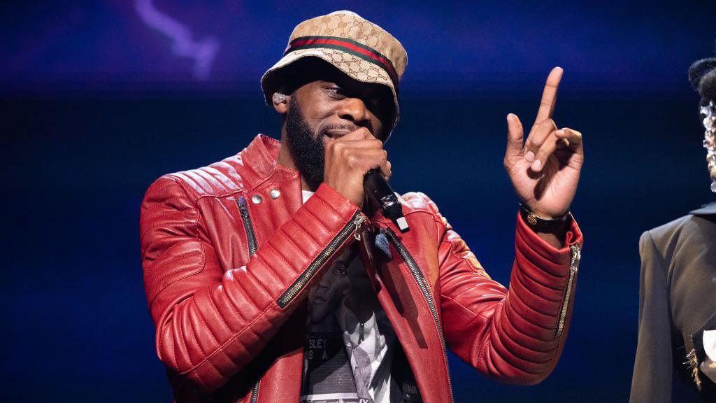 Singer Pras Michel wears a Gucci bucket had and red leather jacket while he performs onstage with The Fugees at Crypto.com Arena in Los Angeles in 2023.