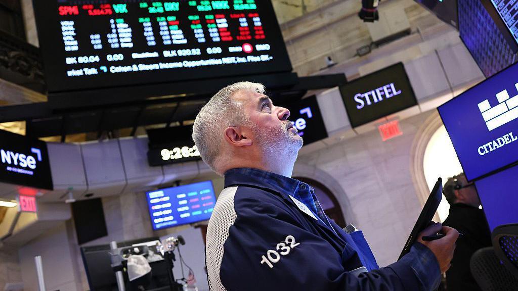A trader looks up at a screen on the floor of the New York Stock Exchange.