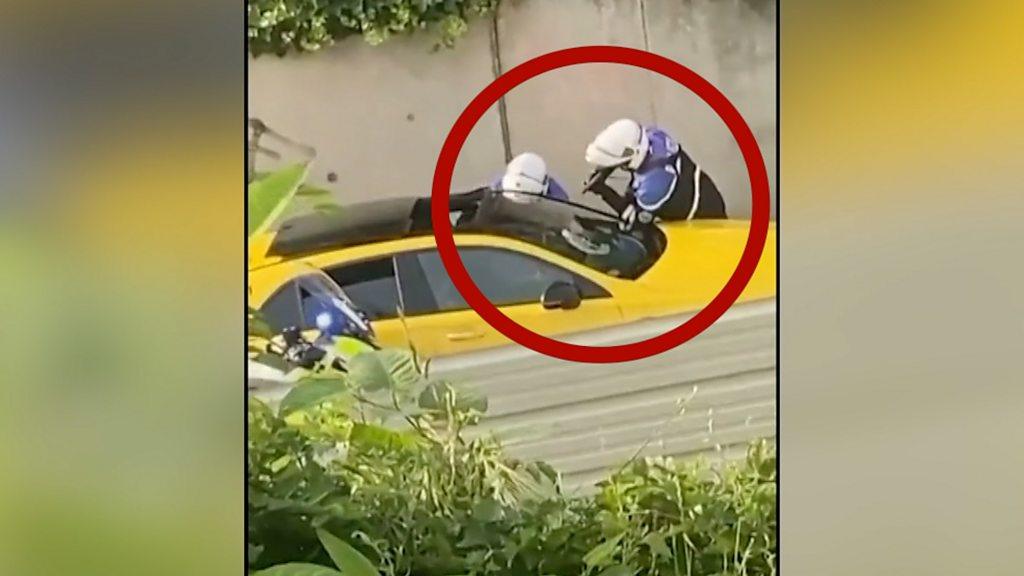 Police surround yellow car, with one officer pointing their gun in the window