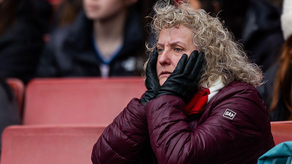An Arsenal fan cuts a glum figure as she watches on from the stands