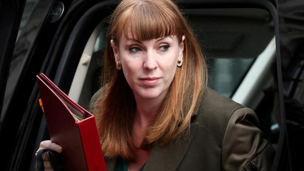 Rayner steps out of a black car carrying a red folder