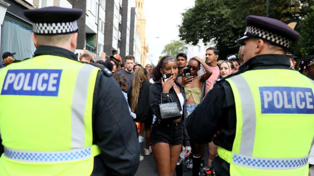 Police stand in the crowd at carnival with the backs to the camera wearing fluorescent tabards