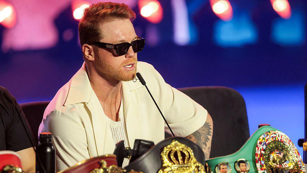 Wearing sunglasses and surrounded by his world titles, Saul Canelo Alvarez speaks at a news conference