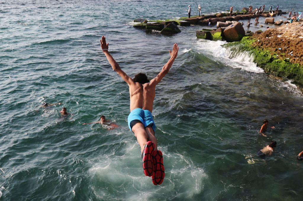 Boys swim at the sea, on of them is diving in.