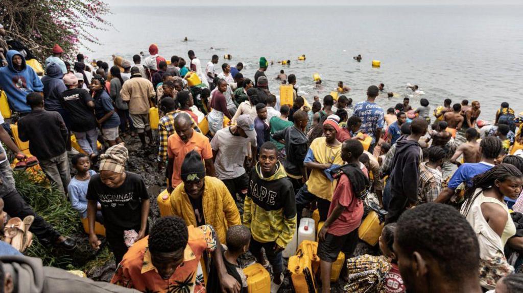 Many people in a crowd carrying their jerrycans as they gather to collect water amid ongoing water shortages at the shore of Lake Kivu in Goma 