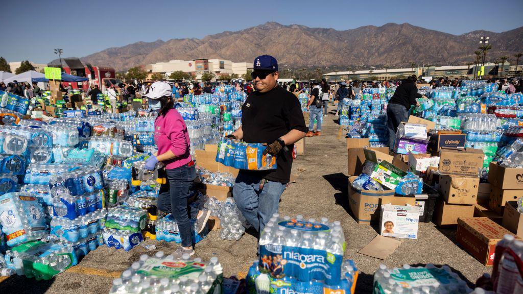 People carry bottles of water in an area filled with water bottles and volunteers