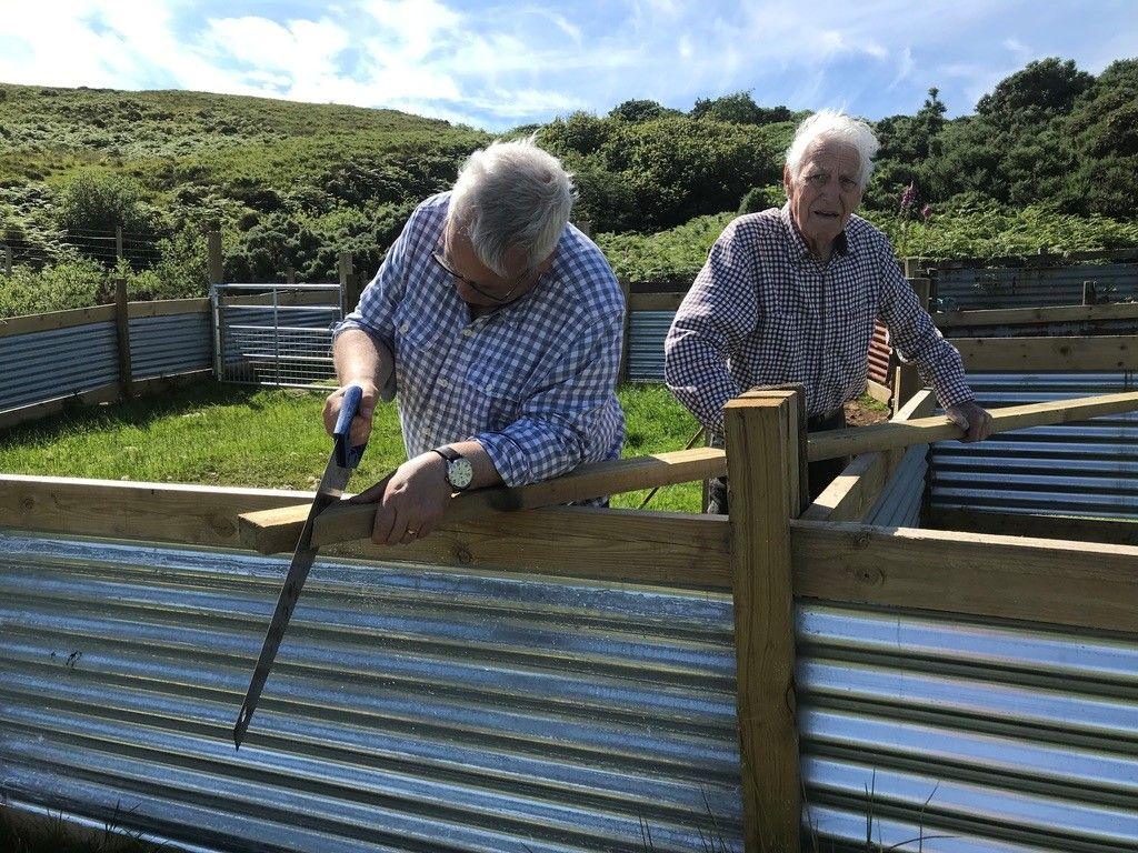 Donnie Dòmhnallach le sàbh a' gearradh pìos fiodha agus athair air a chùlaibh